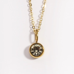 Close-up of gold necklace with round bezel-set crystal pendant on white background