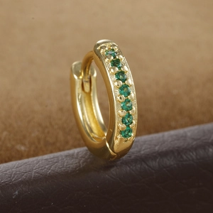 Close-up of golden teardrop earring with round green zircon stone on brown leather