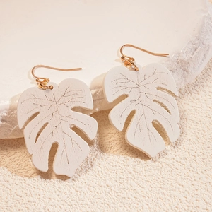 Macro detail of white monstera leaf earrings with gold hooks on stone texture