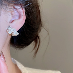 Close-up of bowknot zircon stud earring with silver pin on a female model's ear