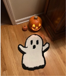 Ghost-shaped plush Halloween doormat on wooden floor with glowing pumpkins