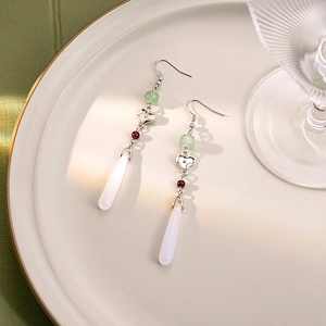 Detail of beaded tassel earrings with white teardrop pendant and green beads on a ceramic plate