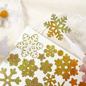 Detailed view of gold glitter snowflake stickers being applied with tweezers for DIY crafts