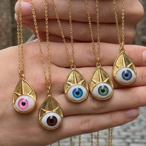 Hand holding five teardrop Evil Eye pendant necklaces in various colors with gold plating