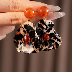 Close-up of resin leopard print flower earrings with warm amber beads on a brown backdrop