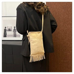 Detail of beige suede crossbody bag with long tassels shown on a black blazer