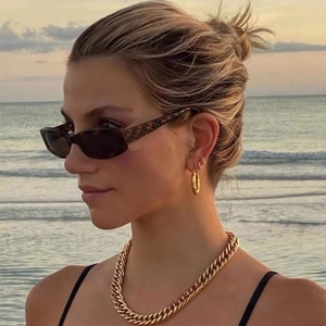 Close-up of chunky gold-plated Cuban link chain and hoop earrings on beach background