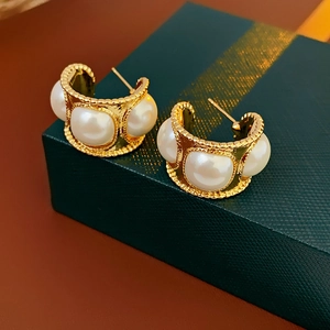 Close-up of vintage C-shape gold earrings with white pearls and beaded metal details