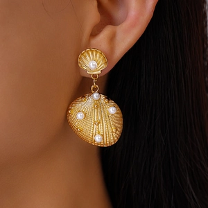 Detail of gold shell drop earring with pearls worn by a model to show size and scale