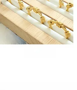 Detailed close-up of golden twisted knot rings displayed on a white textured stand