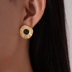 Vue macro de boucles d'oreilles dorées avec textures concentriques et pierre noire carrée