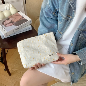 Detailed embroidery of yellow daisies on a beige fabric cosmetic storage bag