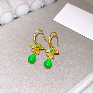 Macro detail of gold floral hook earrings with emerald green teardrop resin stones