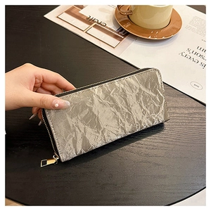 Close-up of a silver metallic pleated long wallet with zipper being held by a model