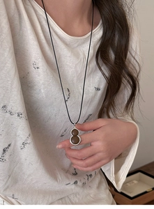 Detail of a resin gourd pendant with bronze frame on a black woven long necklace