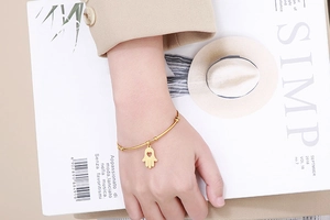Detail of gold Fatima hand charm with hollow heart on a sleek stainless steel bangle