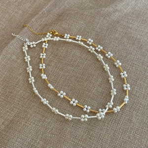 Minimalist pearl flower bead necklace set with gold and silver chains on burlap background
