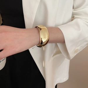 Dettaglio del bracciale rigido dorato minimalista con design geometrico ritorto e lucido