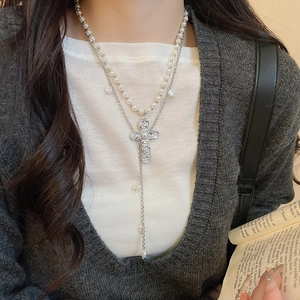 Détail d'un collier à deux couches avec des perles et un pendentif croix argenté vintage