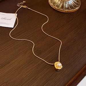 Close-up of irregular pearl pendant with gold snake chain on a vintage wooden surface