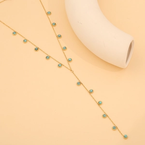 Détail du collier doré en Y avec perles turquoise sur support en céramique