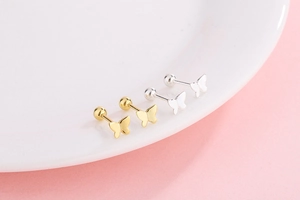 Macro view of gold and silver butterfly screw back stud earrings on white ceramic