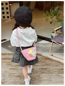 Rear view of a girl wearing a pink woven crossbody bag with flowers and smiley face charms