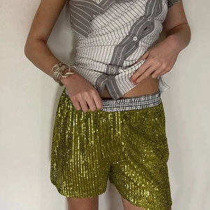 Detailed view of green sequined shorts featuring a black and white checkered elastic waistband