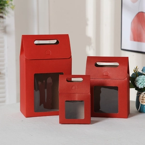 Three red gift boxes with transparent windows and handles in various sizes on a white table