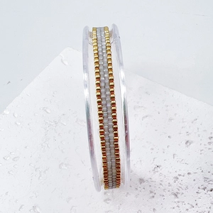Detailed macro view of handmade gold and white beaded bracelet on minimalist stand