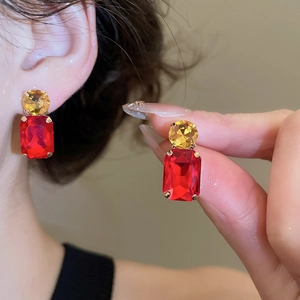 Detail of elegant earrings with round yellow and rectangular red crystals in gold claw setting