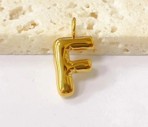 Macro shot of 3D golden puffed letter F pendant on beige stone and white background