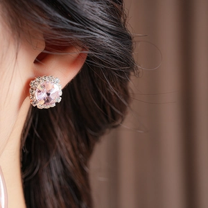 Close-up of sparkling pink crystal stud earrings with diamond halo on model's ear