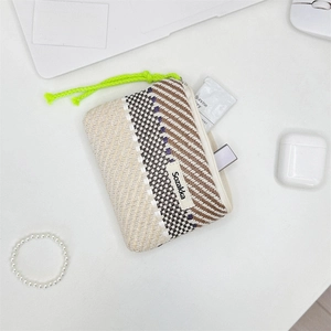 Detail view of a striped knit makeup pouch with green drawstring on a clean white desk