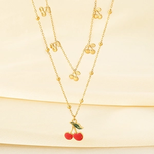 Collier double rang doré avec pendentifs cerises rouges sur fond de soie beige