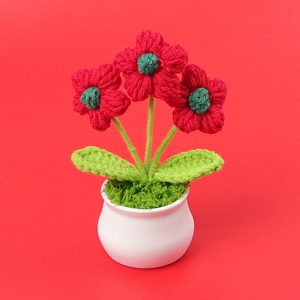 Close-up of handmade crochet mini flower pot with three red flowers in a white ceramic base