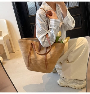 Detail of large straw tote bag with brown leather shoulder straps and woven texture