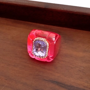 Macro shot of a magenta resin ring with purple gemstone and gold detailing on wood