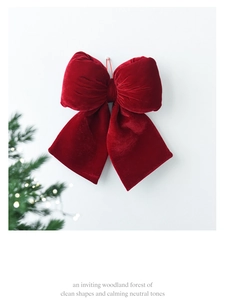 Detail of a large red velvet Christmas bow hanging with festive pine branch and lights