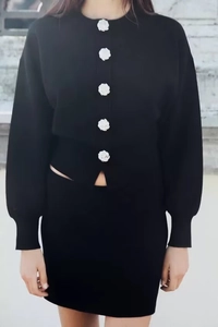 Close-up of black knit cardigan featuring elegant white rose-shaped buttons and texture