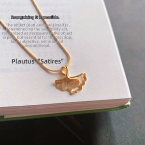 Collana con ciondolo foglia di ginkgo dorata su un libro, gioiello elegante in titanio