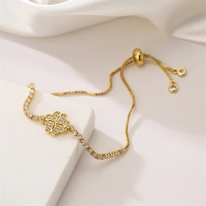 Close-up of golden adjustable bracelet with sparkling clover design on white silk base