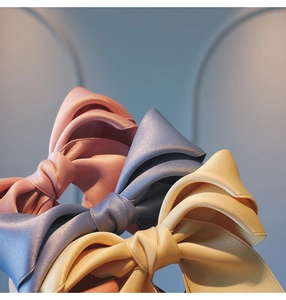 Detail of satin bow hair clips in pink, blue, and champagne with smooth silk texture