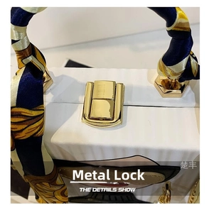 Detail show of golden metal lock and printed silk scarf handle on white box bag