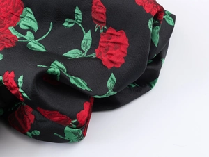 Gros plan détaillé du tissu satiné jacquard avec roses rouges et feuilles vertes