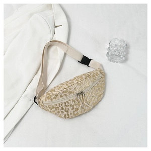 Detail of woven straw fanny pack with golden texture and adjustable strap on white blazer