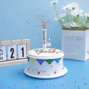 Musical confetti birthday candle spraying colorful paper on a cream cake background