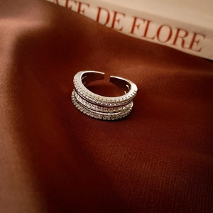 Elegant silver zircon triple-layer open ring displayed on textured brown fabric