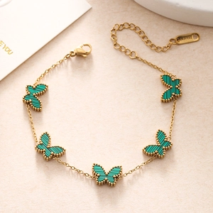 Macro shot of gold double-layer chain bracelet with green butterfly charms and S.STEEL stamp
