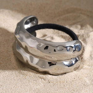 Macro detail of silver liquid metal hair ring with wavy texture on natural sand